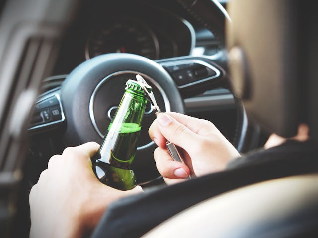 person opening beer bottle in the car